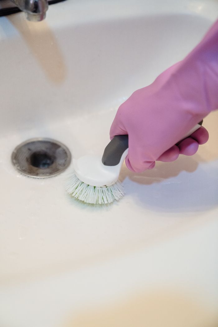 gallery-3 A close-up of a hand in a glove cleaning a sink with a scrub brush.